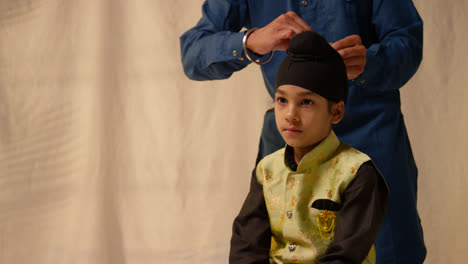 Foto-De-Estudio-De-Un-Padre-Atando-Un-Turbante-En-La-Cabeza-De-Su-Hijo-Sikh-Que-Lleva-Un-Chaleco-Tradicional,-Como-Se-Muestra-En-La-Secuencia,-Parte-7-De-10